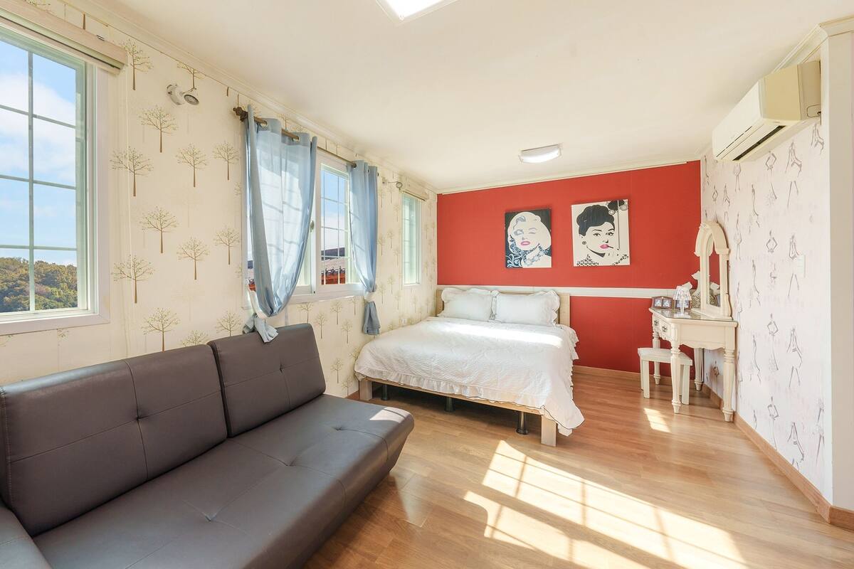 A bedroom with a bed, a sofa, a dresser, and a window with curtains.