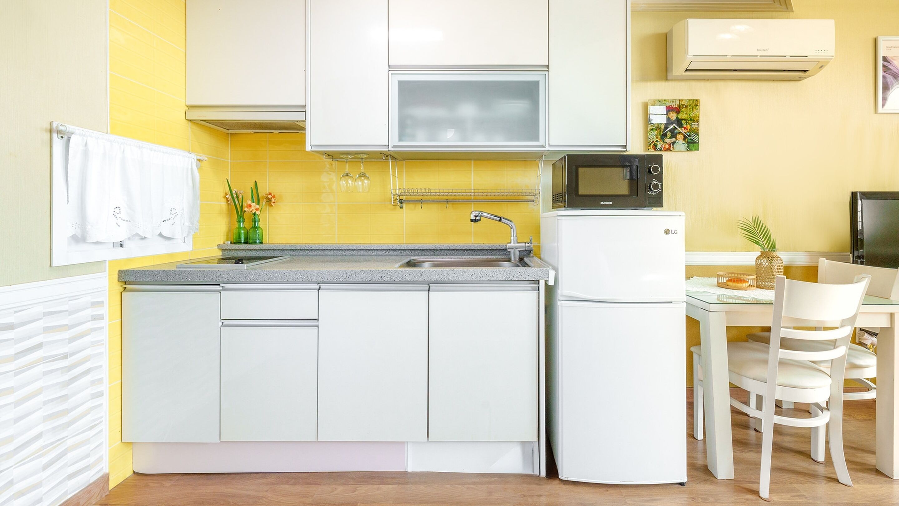 A compact kitchen with white cabinets, a microwave, a refrigerator, and a dining area with a table and chairs.