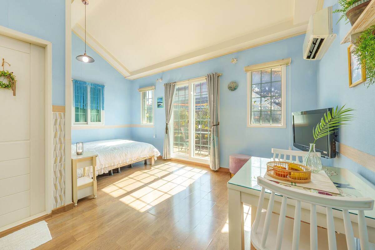 A bright room with a bed, a TV, and a dining area.