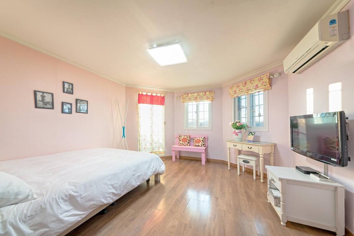 A bedroom with a bed, a desk, a television, and an air conditioning unit.