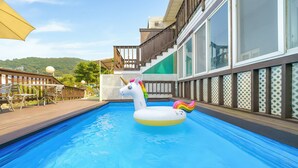 Una piscina con un flotador de unicornio, terraza de madera y mobiliario exterior.