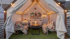 Un espace accueillant aménagé sous une tente, avec une table, des chaises et une fresque représentant un terrain de camping.