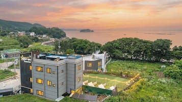 Un edificio moderno con piscina en la azotea, rodeado de vegetación exuberante y vistas al mar.