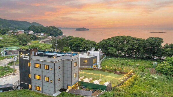Un edificio moderno con piscina en la azotea, rodeado de vegetación exuberante y vistas al mar.