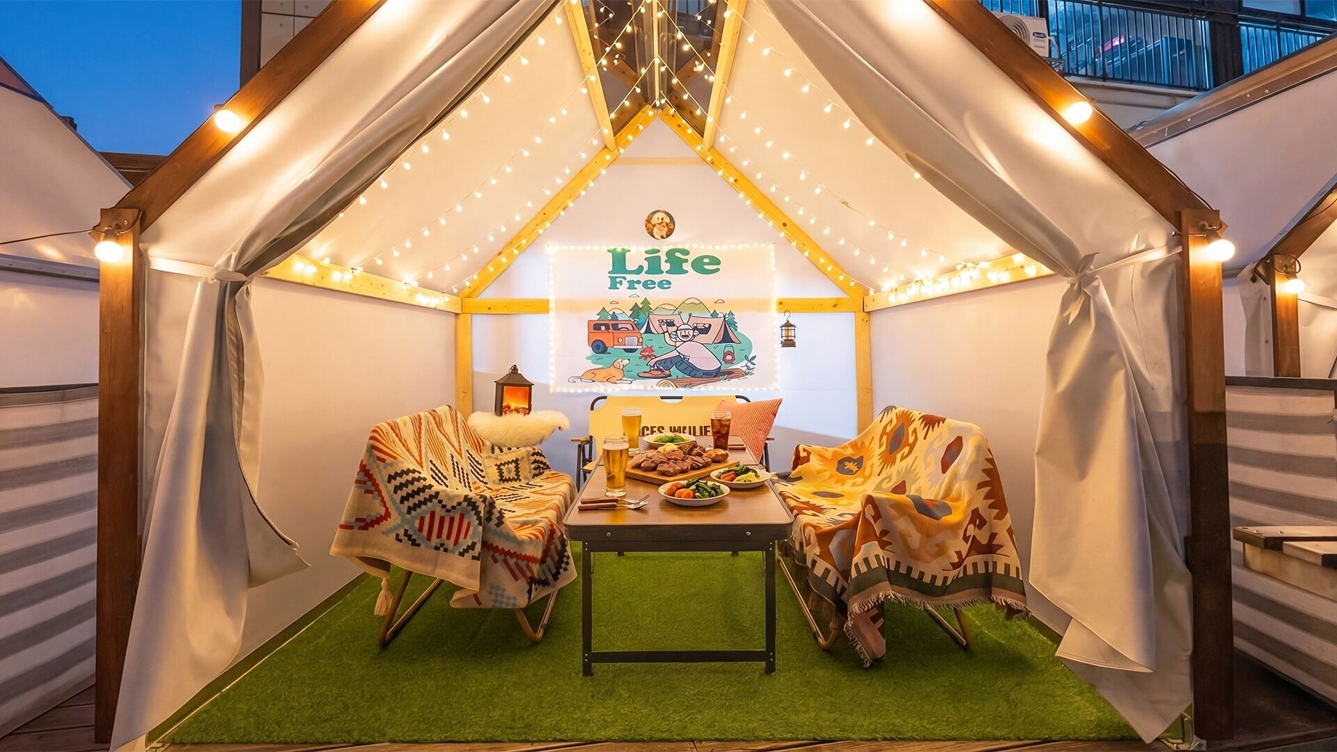 Eine zeltähnliche Konstruktion mit einem 'Life Free' Schild, einem Tisch mit Essen und einer Laterne.
