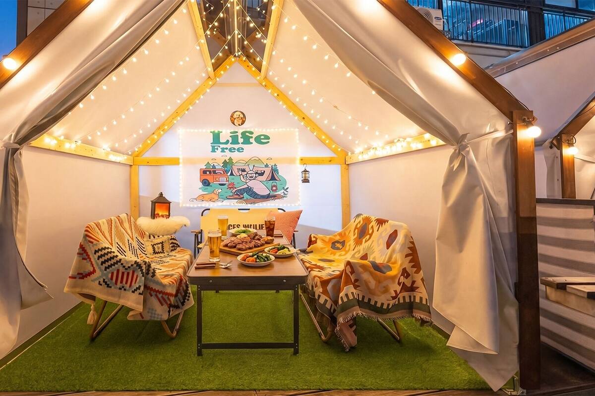 A tent-like structure with a 'Life Free' sign, a table with food, and a lantern.
