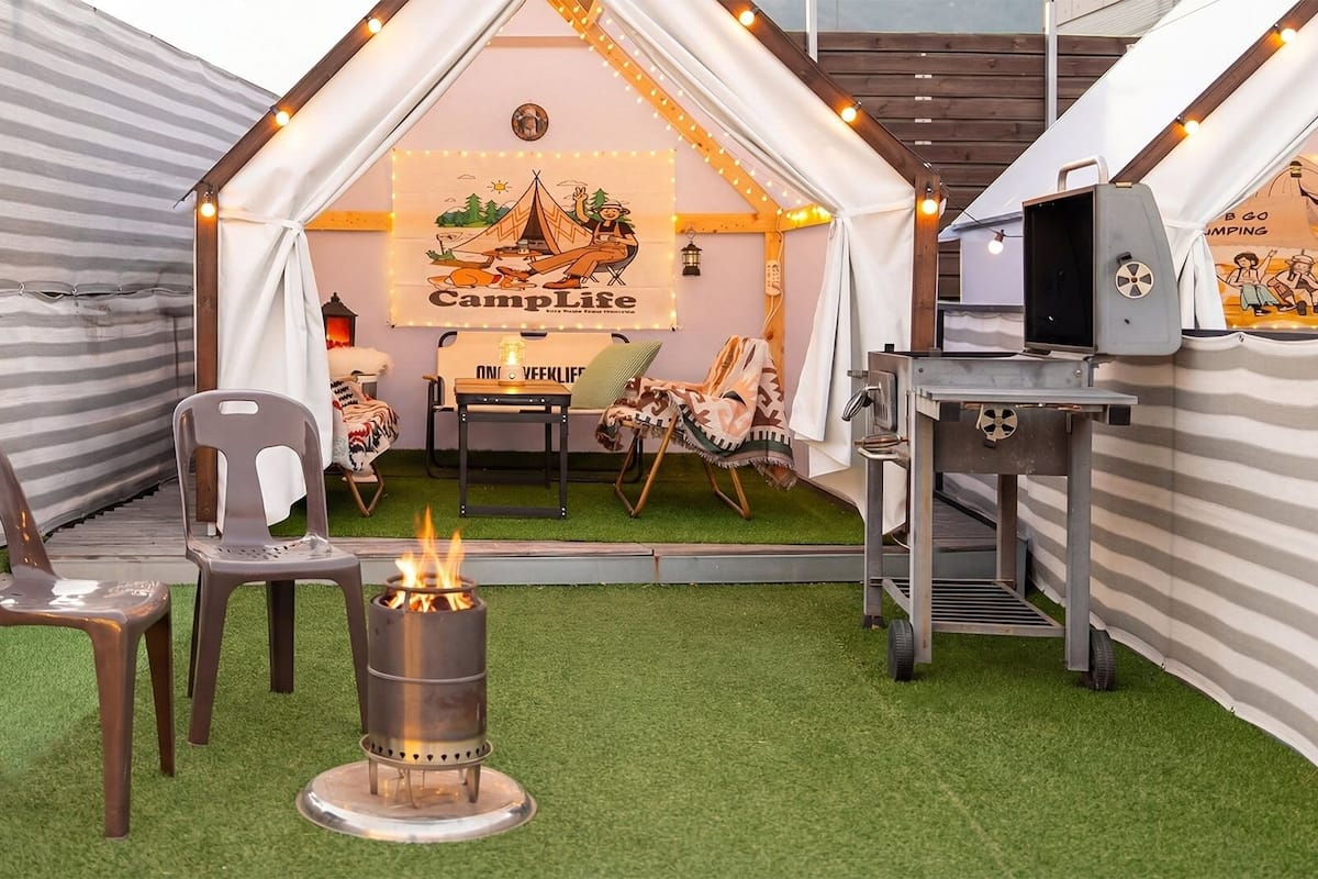 A cozy indoor camping area with a tent, chairs, a campfire, and a grill.