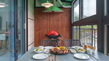 A dining area with a grill, a table set with plates, bowls, and cutlery, and a view of the outdoors through large windows.