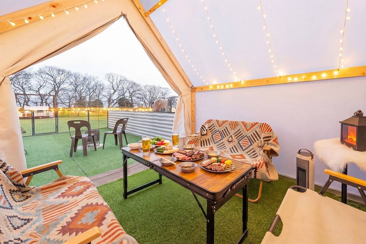 A tented outdoor dining area with a table set for a meal, chairs, a lantern, and a view of the outdoors.