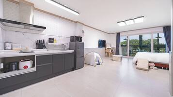 A modern kitchen with a built-in stove, microwave, and refrigerator. There is a tent set up in the living area, and a bed with a view of the outdoors.