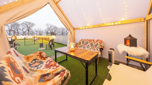 A tent with a table, chairs, and a view of a fenced outdoor area.