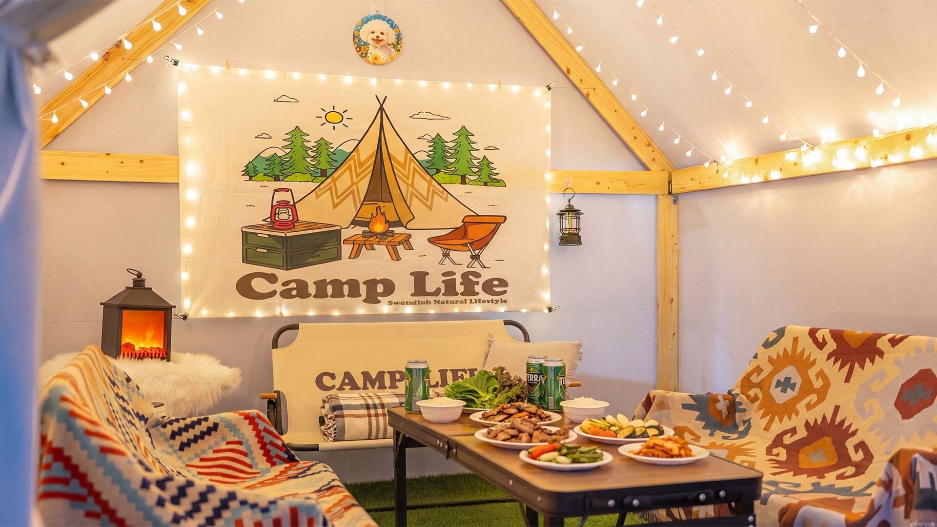 Gemütliches Zeltinnere mit einem 'Camp Life'-Banner, einem Lagerfeuer und einem Tisch mit Lebensmitteln.
