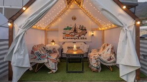Una habitación tipo tienda de campaña acogedora, con un mural, dos sillas, una mesa y luces colgantes.