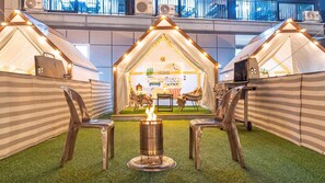 Un espace aménagé sur le thÚme du camping, avec des tentes, un feu de camp et des chaises de camping.
