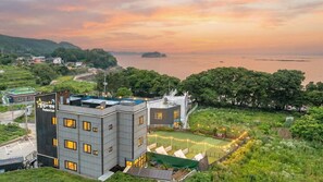 Un edificio moderno con piscina en la azotea, rodeado de vegetación y vistas al mar.