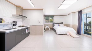Habitació d'hotel moderna amb petita cuina, un llit amb estructura de tenda i una finestra gran amb vistes.