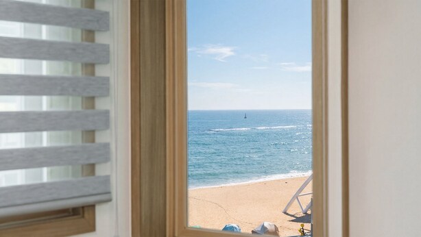 A window view of a beach with a chair and a hat on the sand. - Sokcho Harmony Pension (Sokcho)