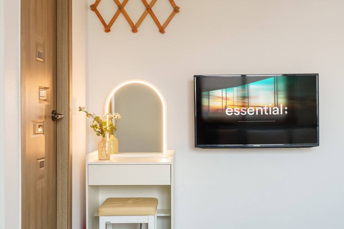 A modern bathroom with a vanity, a mirror with a light, and a TV displaying the word 'essential'.