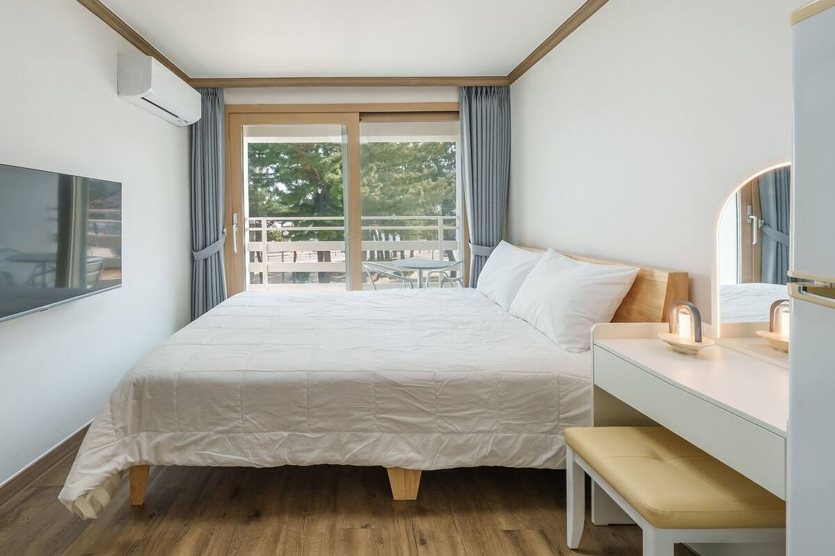A hotel room with a bed, a desk, a chair, a TV, and a balcony with a view.