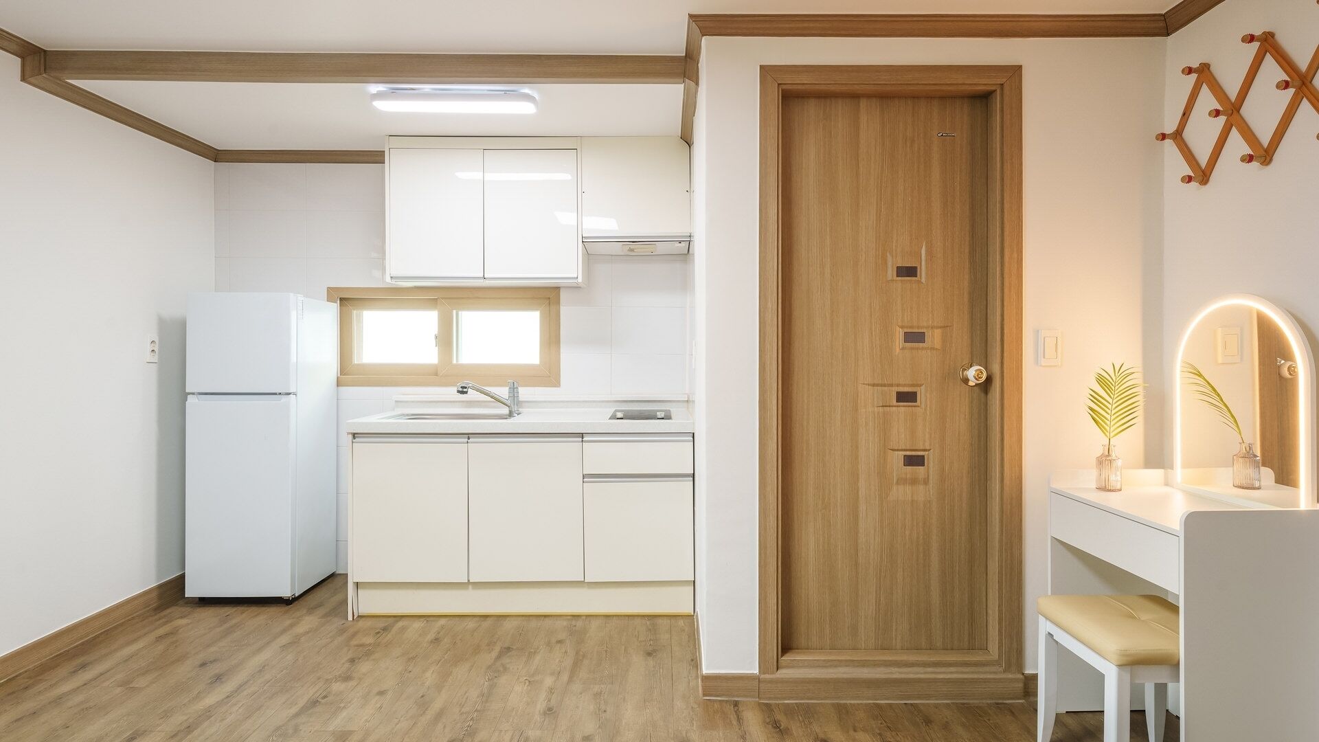 A compact kitchen with white cabinets, a wooden door, and a small vanity with a mirror.