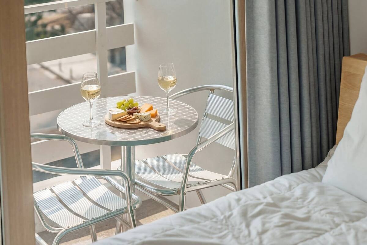 A hotel room with a bed, a balcony with a table and chairs, and a view of the outside.