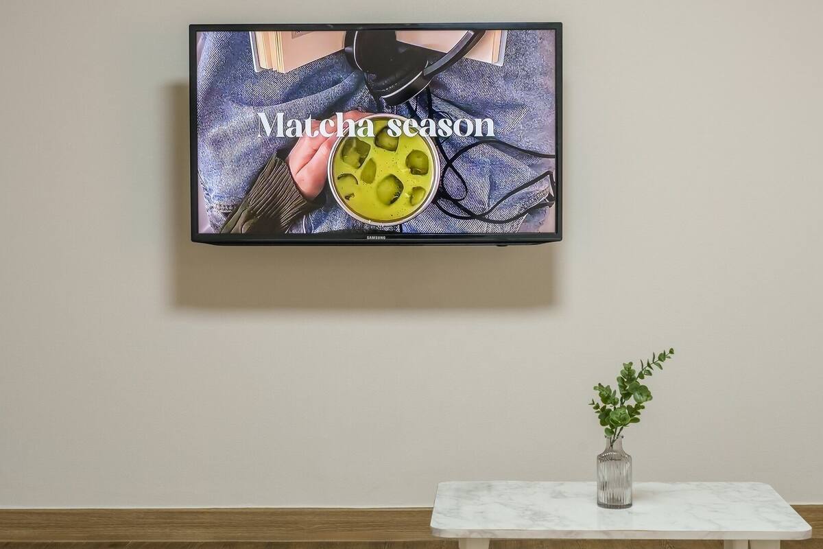 A television mounted on a wall displaying a person holding a yellow object with the text 'Matcha season' visible.