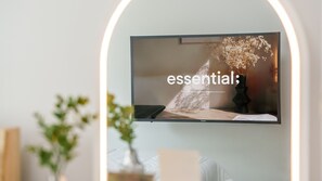 A flat-screen TV mounted on a wall with a decorative vase and flowers. - Sokcho Harmony Pension (Sokcho)