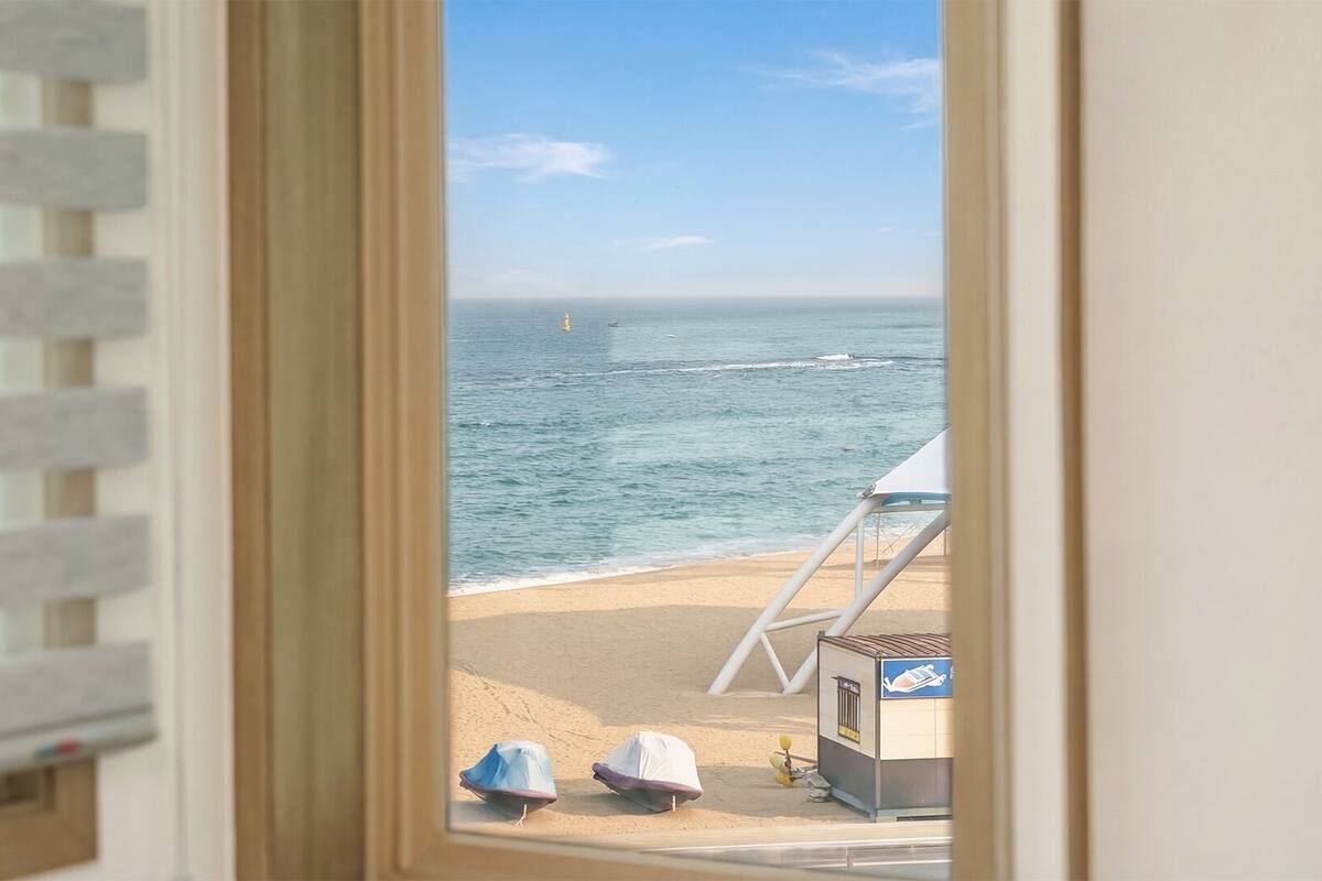 A beach view through a window with a beach umbrella and a lifeguard stand.