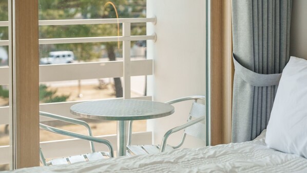 Habitación de hotel con cama, una mesita redonda y un balcón con barandilla.