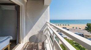 Ein Balkon mit Tisch und Stuhl mit Blick auf einen Strand, auf dem Autos und Sonnenschirme geparkt sind.