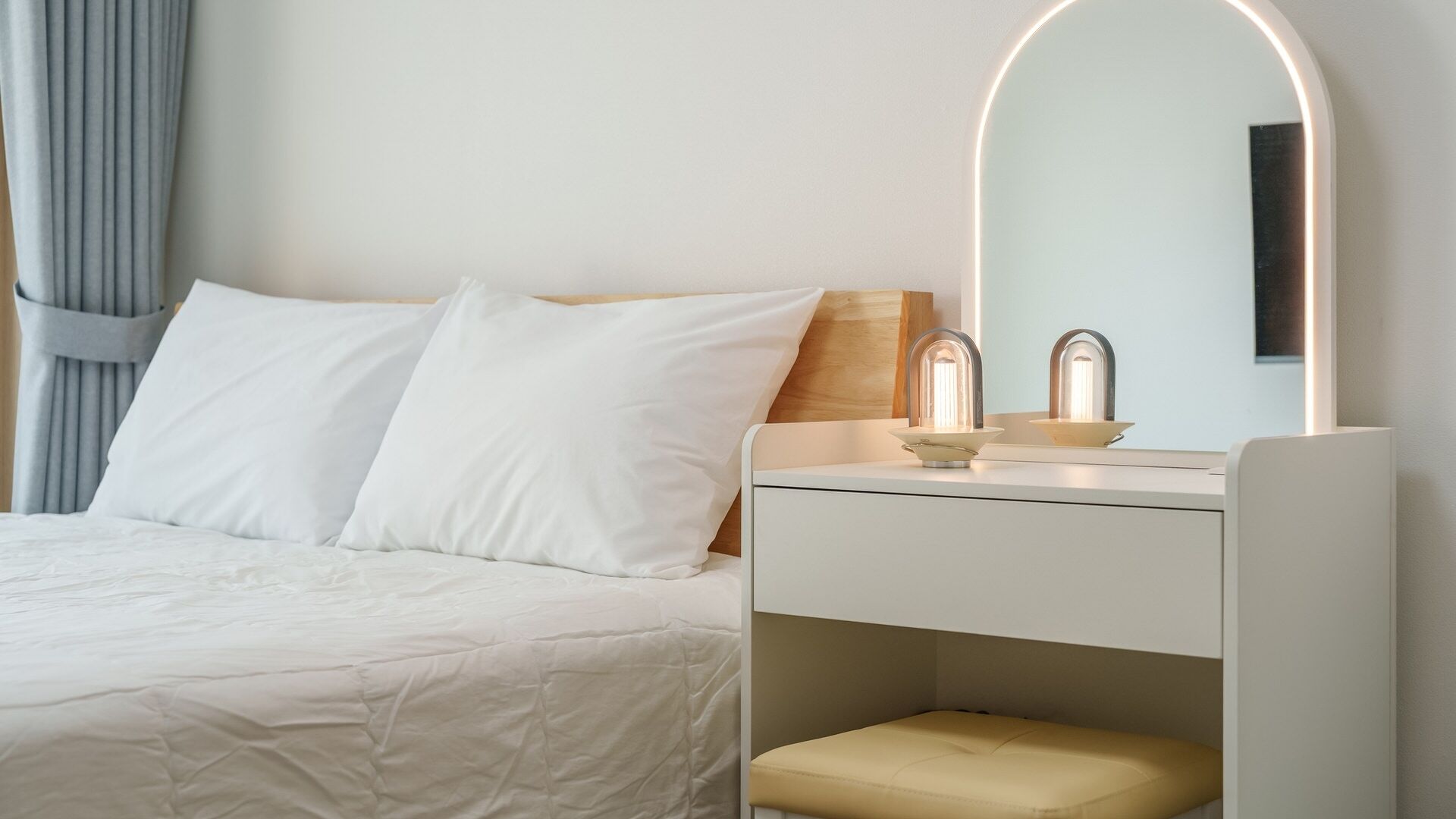 Ein Hotelzimmer mit Bett, Nachttisch mit Spiegel und einem kleinen Hocker.