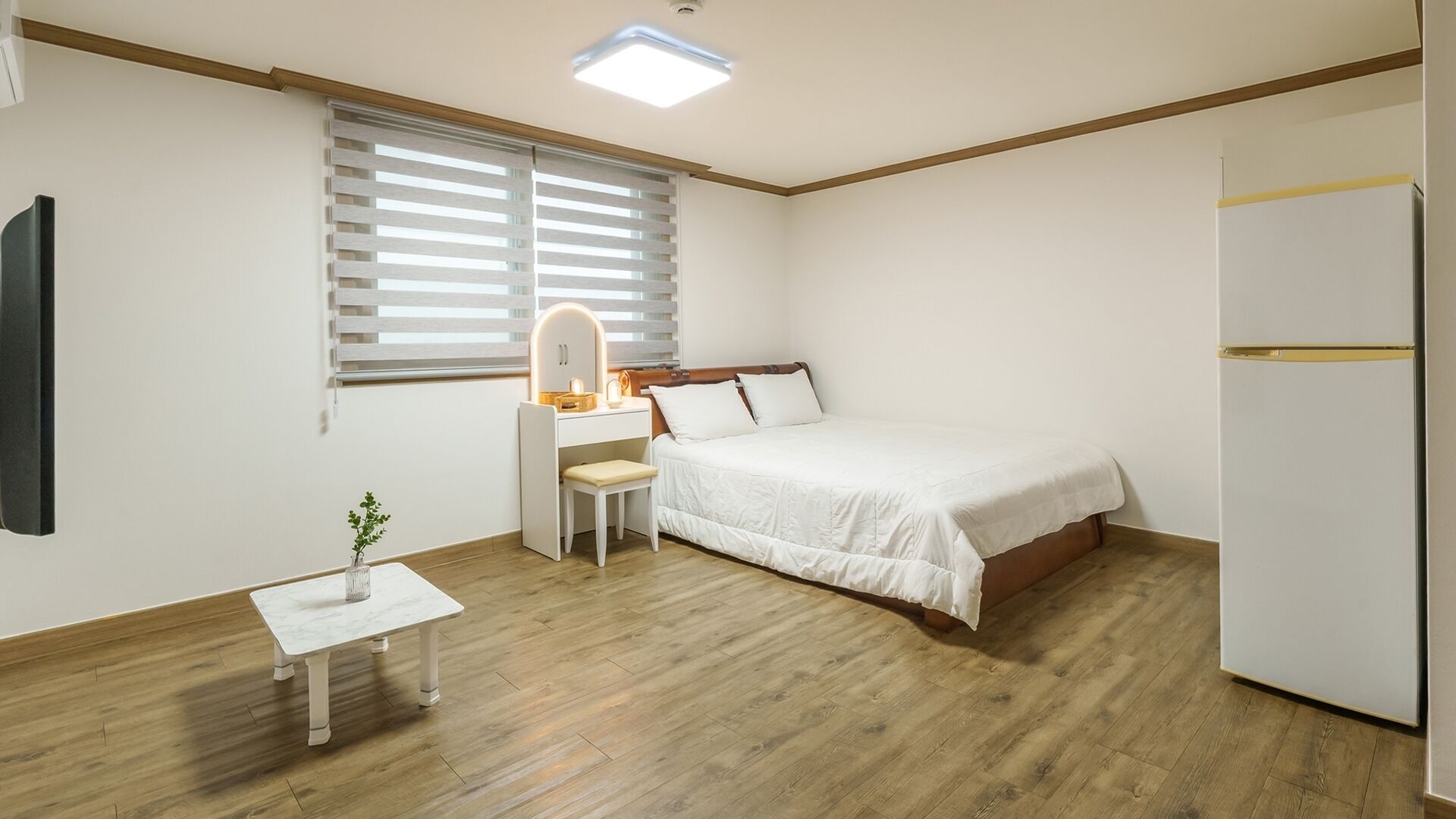 Un dormitorio con cama, escritorio, silla, mesita de noche y refrigerador.