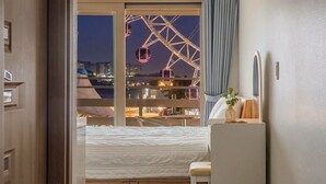 A hotel room with a bed, a desk, a chair, a window with a view of a Ferris wheel, and a curtain. - Sokcho Harmony Pension (Sokcho)
