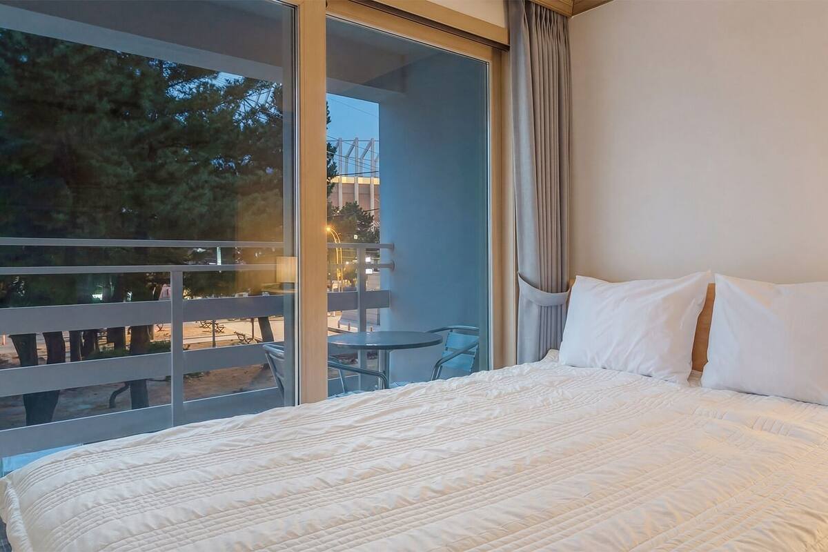 A hotel room with a large bed, a balcony with a table and chairs, and a view of the outdoors.