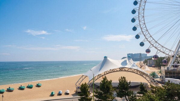 A beach with a large Ferris wheel, a tented area, and a clear view of the ocean.