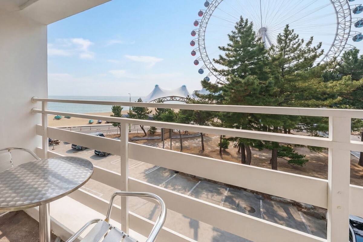 A balcony with a view of a beach, a Ferris wheel, and a parking area.