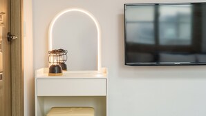 A modern bathroom with a white vanity, a curved mirror with LED lighting, a Samsung TV mounted on the wall, and a wooden door. - Sokcho Harmony Pension (Sokcho)