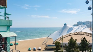 A beach view with a white umbrella structure, a building with a green roof, and a clear sky. - Sokcho Harmony Pension (Sokcho)