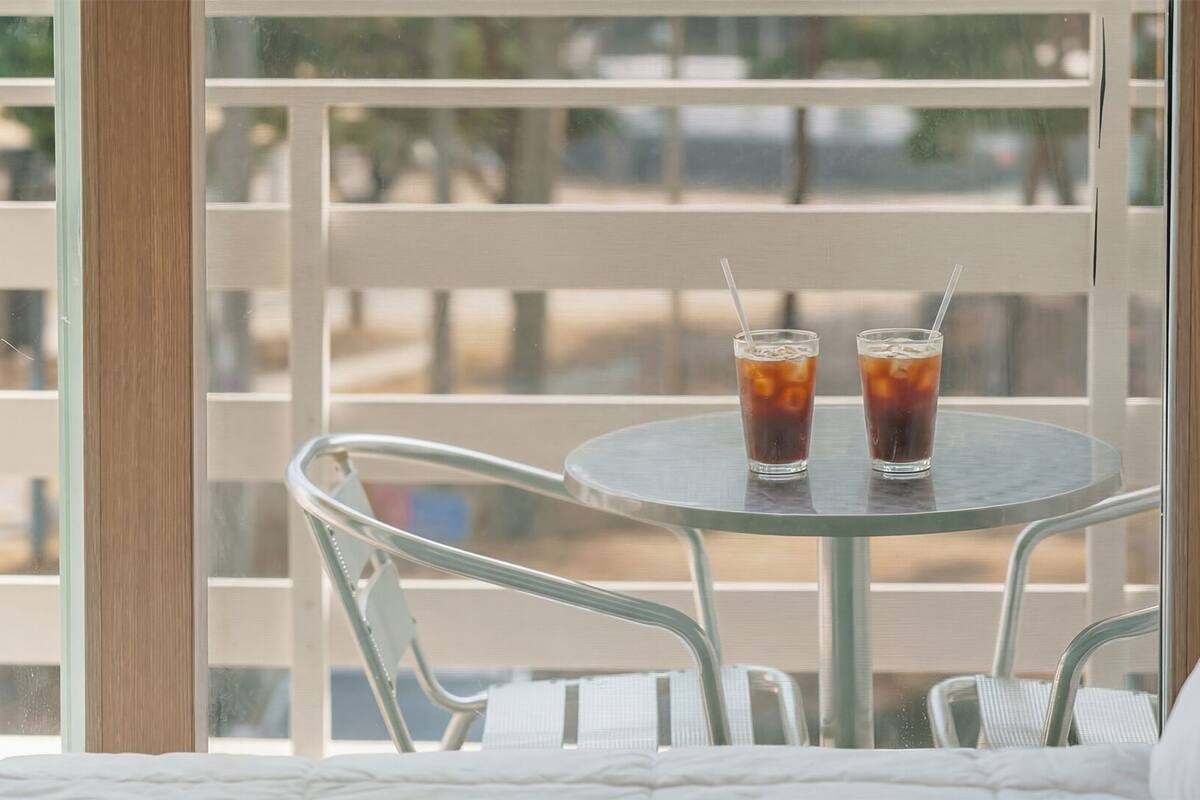 A round metal table with two glasses of iced tea, a metal chair, and a view of a wooden deck through a window.