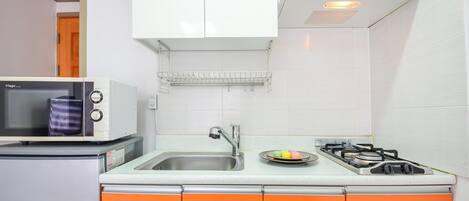 A compact kitchen with a microwave, a small refrigerator, a sink, and a gas stove.