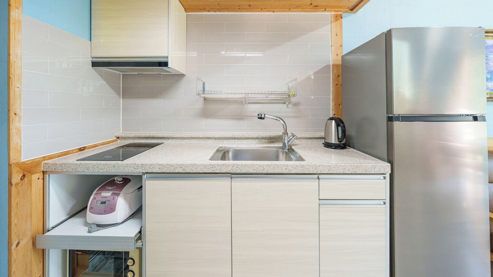 A modern kitchen with a stainless steel refrigerator, a built-in oven, and a sink with a kettle.