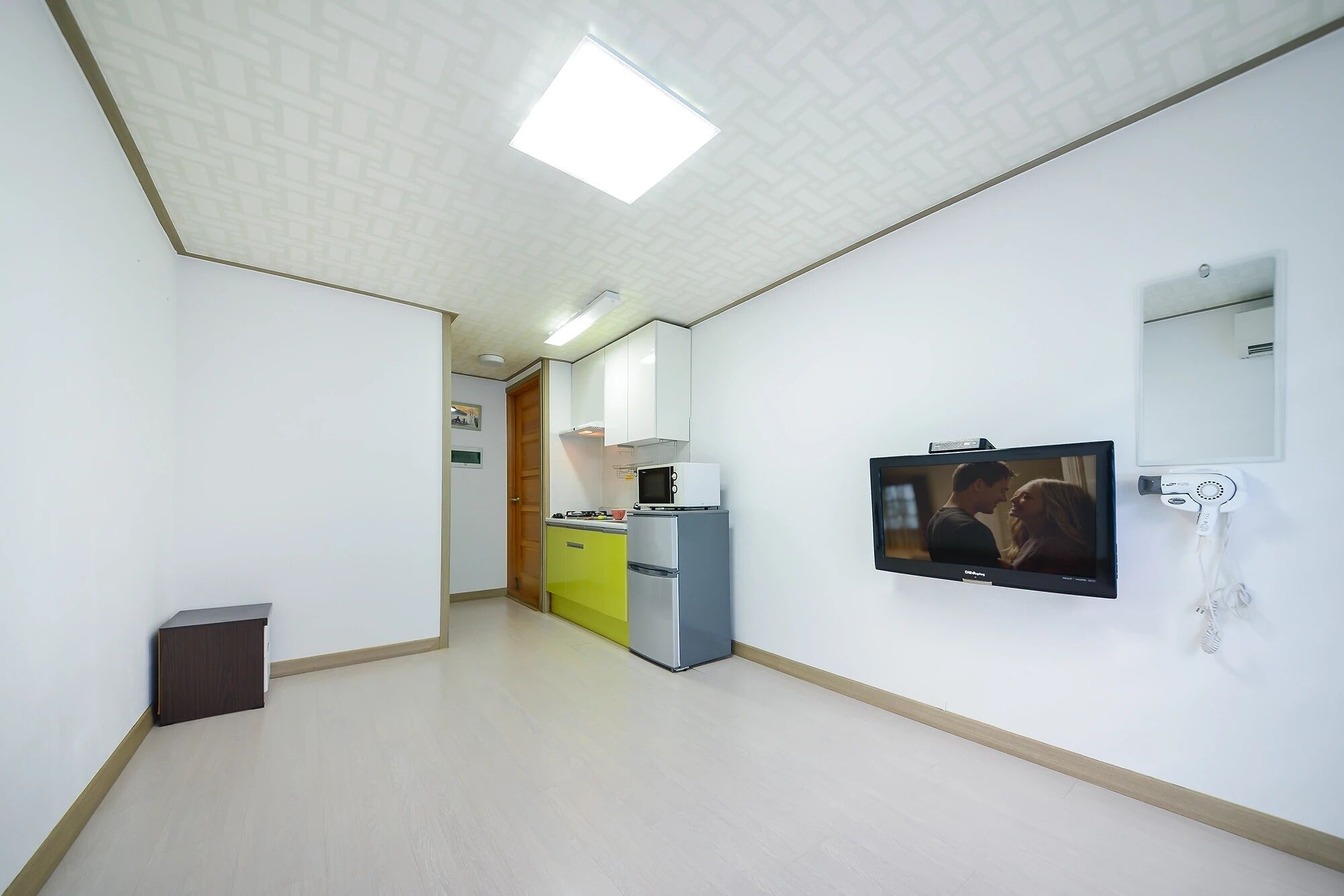 A hotel room with a kitchenette, a television mounted on the wall, and a mirror above the sink.