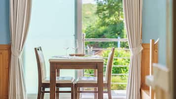 Comedor con una mesa lista para dos personas, una copa de vino y vistas al follaje a través de una ventana.
