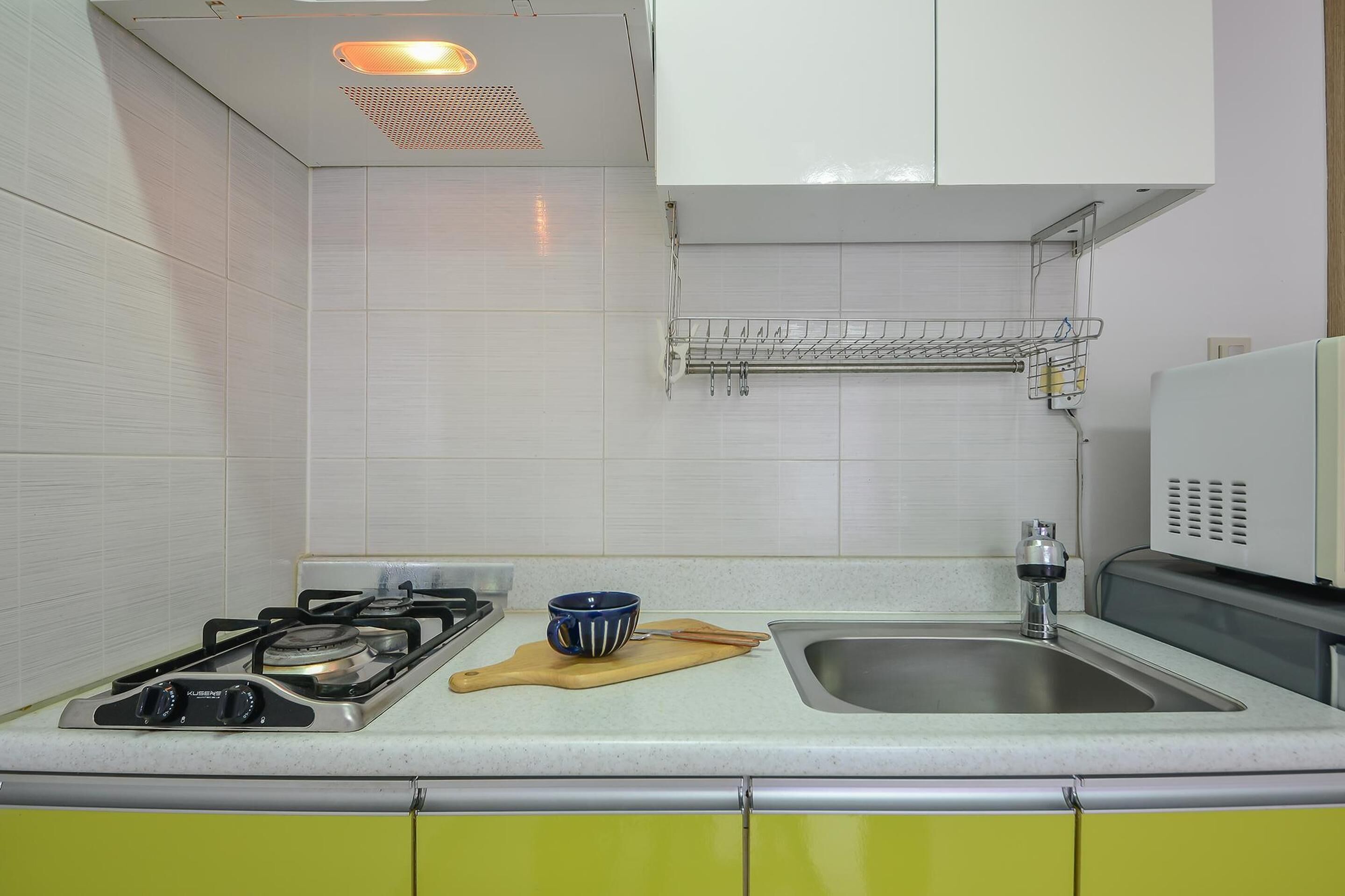 A kitchen with white tiles, a gas stove, a sink, and a microwave.