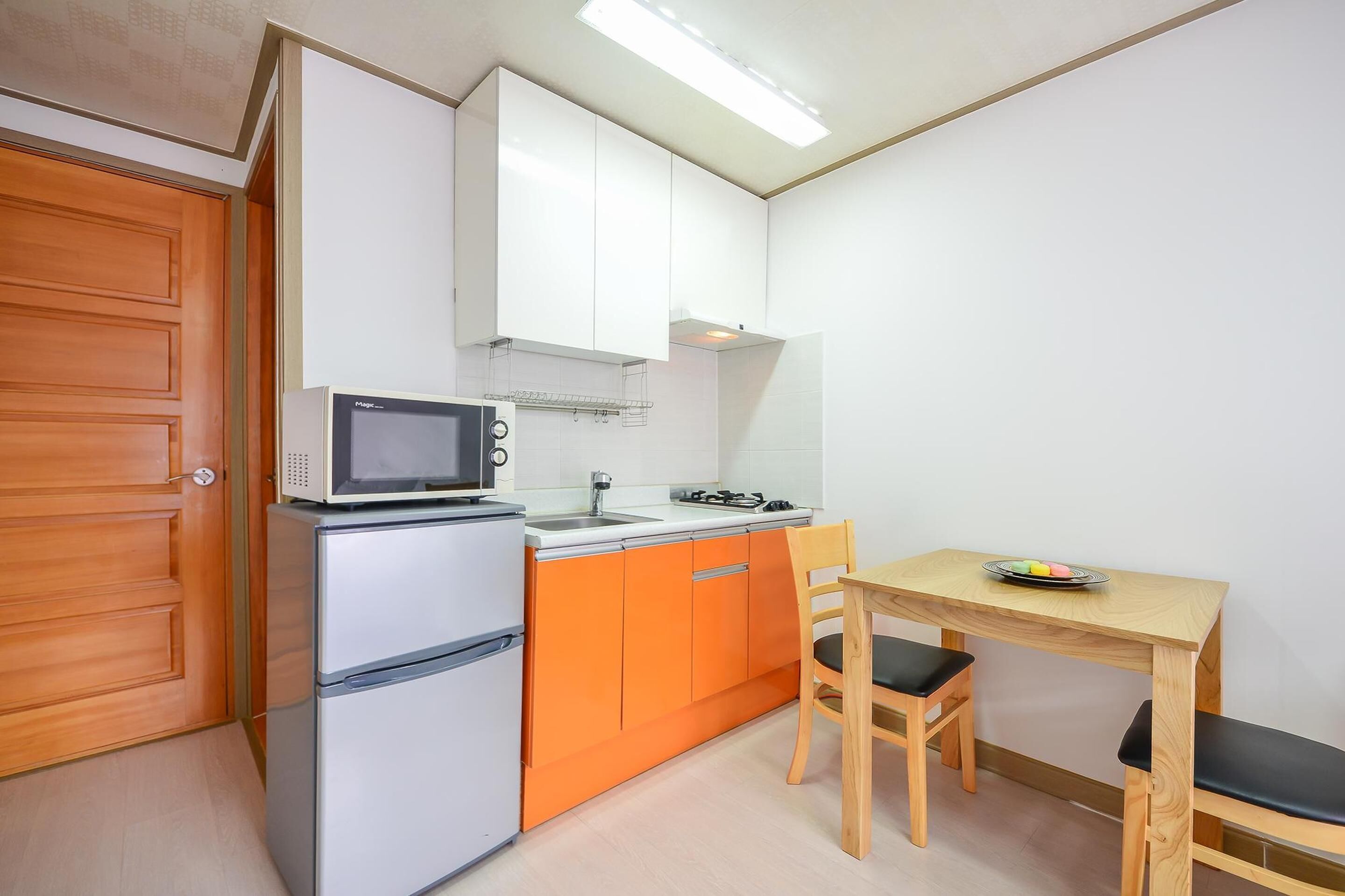 Een kleine keuken met een magnetron, koelkast en oranje kastjes.