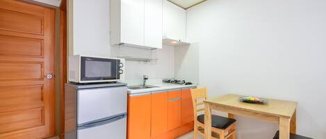 Een kleine keuken met een magnetron, koelkast en oranje kastjes.