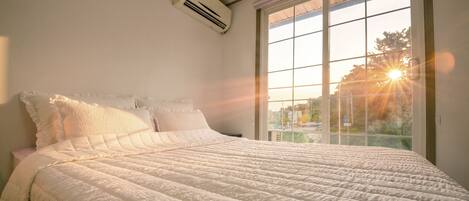 Een bed met een gewatteerde spreidek, een raam met uitzicht en een airconditioning op de muur.