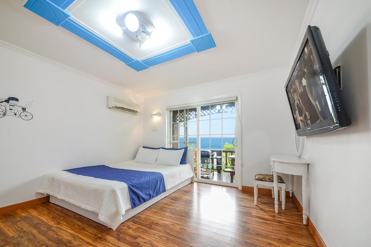 A bedroom with a bed, a TV, a window, and a balcony.
