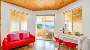 A room with a red sofa, two red chairs, a wooden ceiling, and large windows with a view of the sea. - Geoje Purenneoul Pension (Geoje)