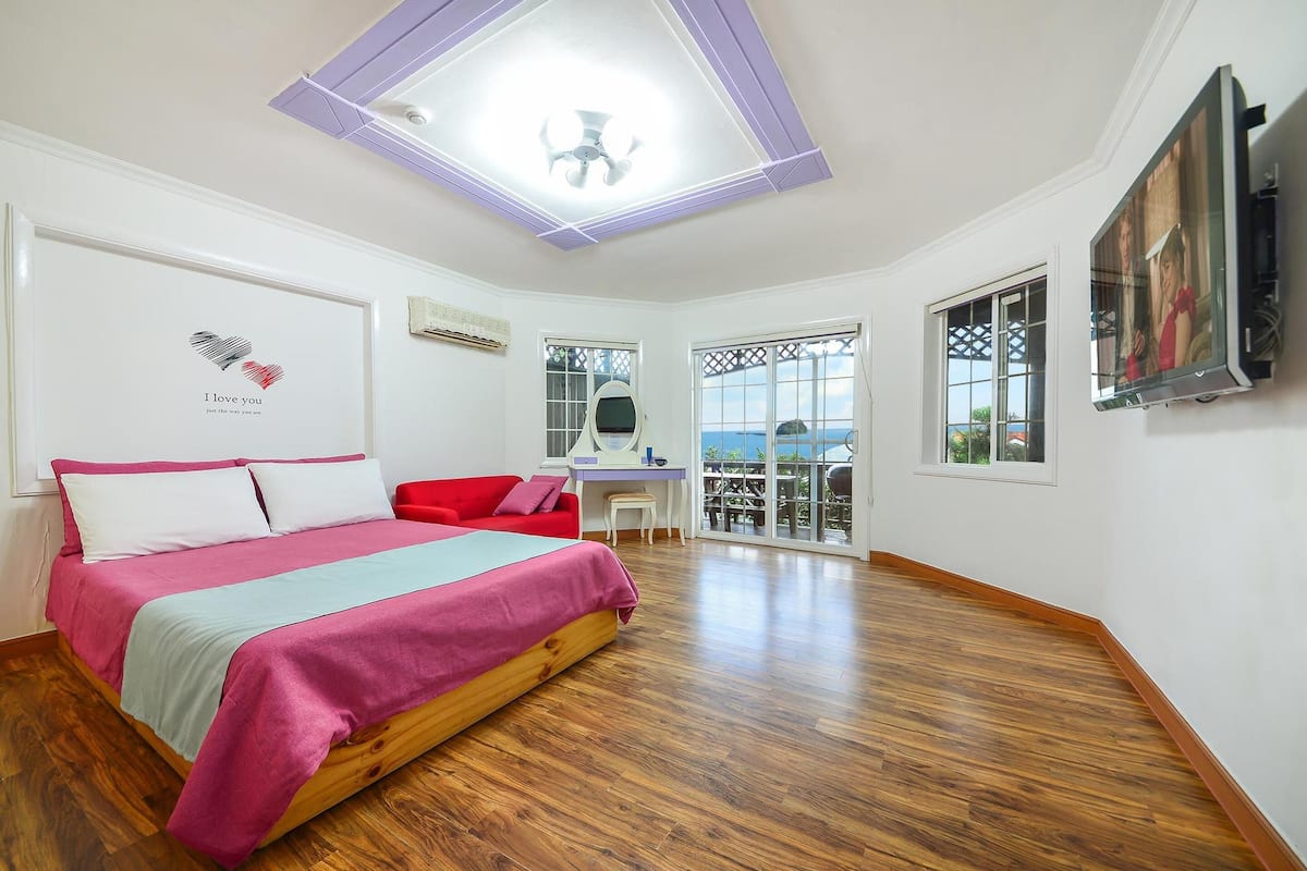 A bedroom with a bed, a desk, and a balcony with a view.